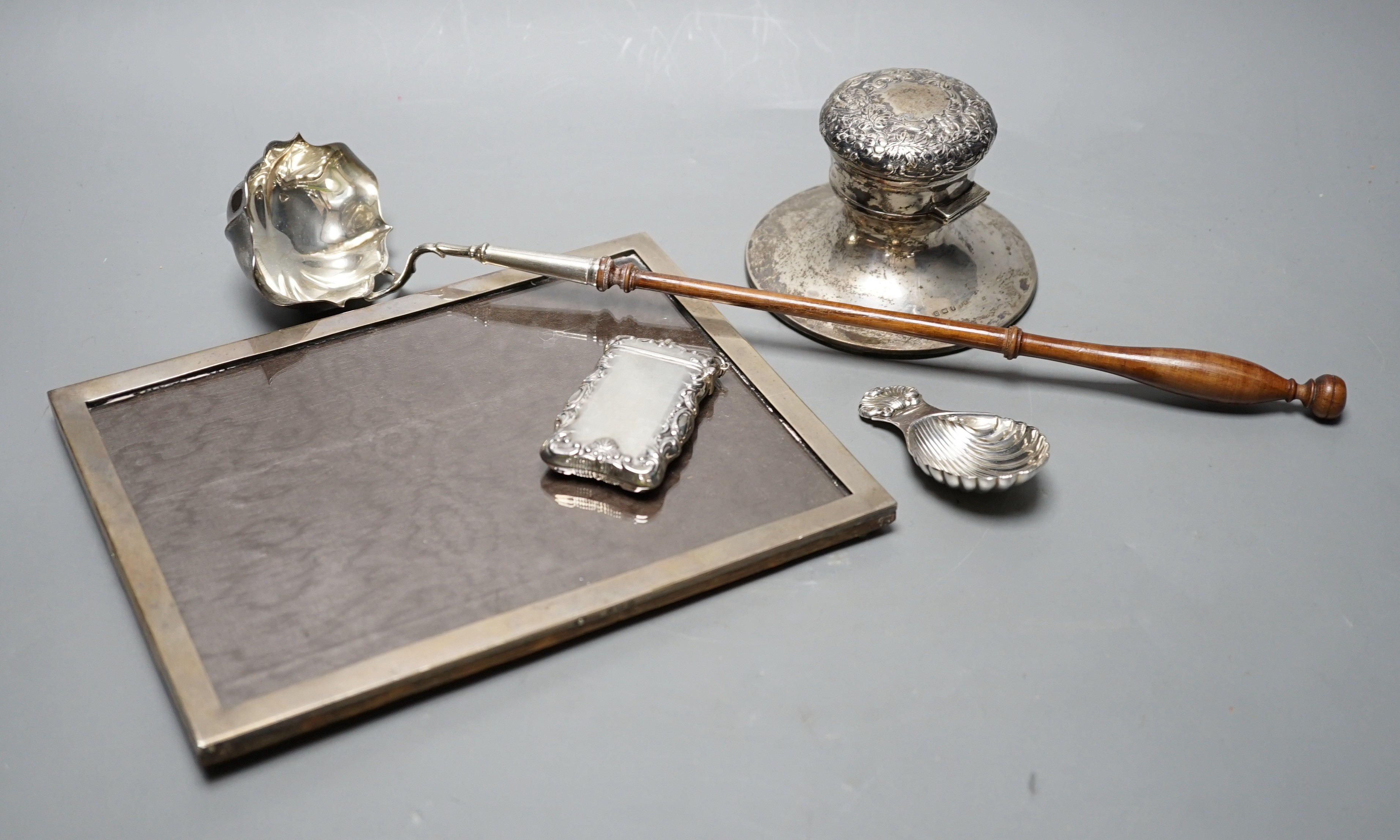 A silver mounted rectangular photograph frame, a modern silver mounted toddy ladle, a silver vesta case, a modern silver caddy spoon and a silver mounted inkwell.